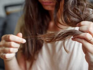 A woman inspecting her hair with some strands falling out
